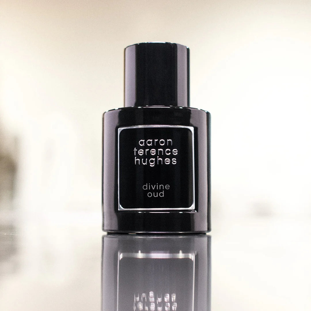 Flacon noir de parfum Divine Oud d'Aaron Terence Hughes sur une surface réfléchissante.